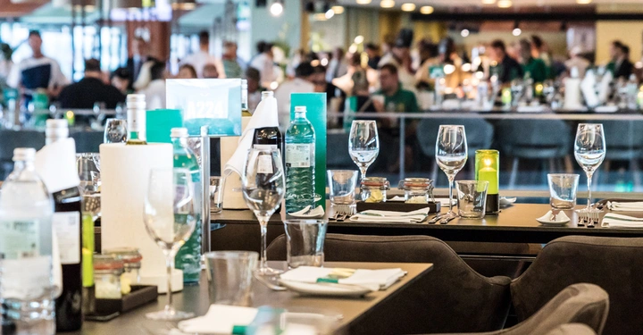 Galerie-Bild 5: Weingläser und Mineralwasserflaschen auf gedecktem Tisch in einem belebten Restaurant mit Menschen im Hintergrund