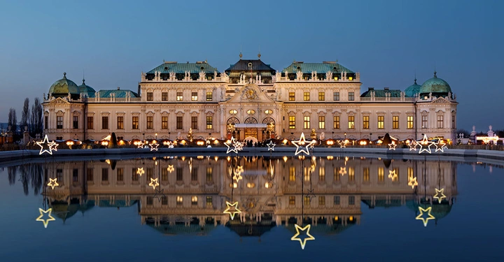 Beleuchtetes Schloss Belvedere zur Weihnachtszeit mit Sternen-Dekoration, die sich im Wasserbecken spiegelt.