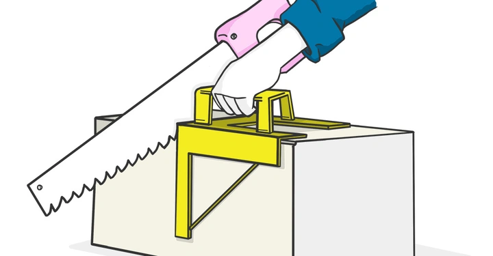 Ein Werkzeug wird von einer Hand mit einer Säge geschnitzt im Hintergrund ist ein großer gelber Kasten mit einem eingelegten Sägeblatt