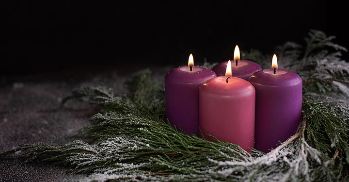 Adventskranz mit lila und rosa Kerzen, die die liturgischen Farben der Kirche und den religiösen Ursprung des Adventsbrauchs symbolisieren.