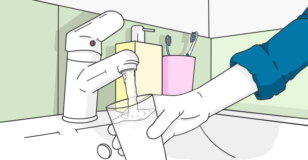 Eine Hand hält ein Glas unter einen fließenden Wasserhahn Waschbeckenbereich mit Zahnbürsten und einem Seifenspender im Hintergrund