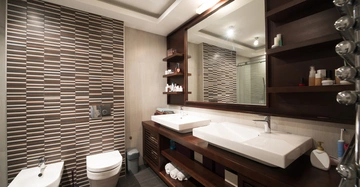 Zwei Waschbecken auf einem Holztisch mit einem großen Spiegel darüber befinden sich in einem modernen Badezimmer mit vielen Regalböden auf der rechten Seite und einer Toilette sowie einem Bidet links.