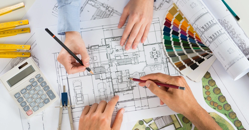 Tisch voll mit Gartenplänen, Grundrissen, Farbfächern, Zollstab, Taschenrechner. Stifthaltende Hände von Menschen, die Pläne besprechen