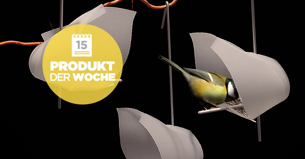 Ein kleiner Vogel pickt an einem Futterspender in Form von Blütenkelchen hängend an einem Ast vor einem schwarzen Hintergrund. Text: 15 PRODUKT DER WOCHE