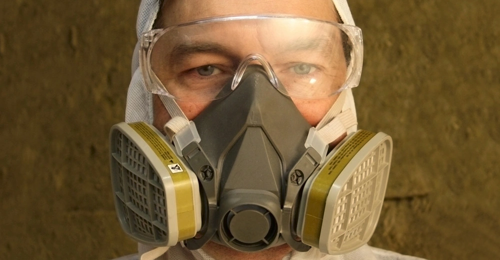 Person trägt eine graue Atemschutzmaske und Schutzbrille in Nahaufnahme offenbar bei einer Arbeit in einer staubigen oder gefährlichen Umgebung