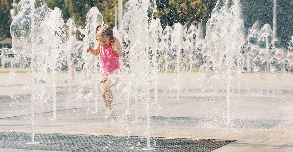 Kind spielt mit Wasser in ausgetrocknetem Stadtbrunnen. Symbolbild für klimabewusste Stadtplanung, Hitzevorsorge und nachhaltige Nutzung urbaner Räume.