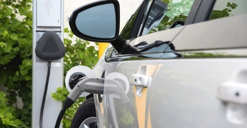 Ein Elektroauto wird aufgeladen an einer Ladestation im Freien umgeben von grünen Pflanzen