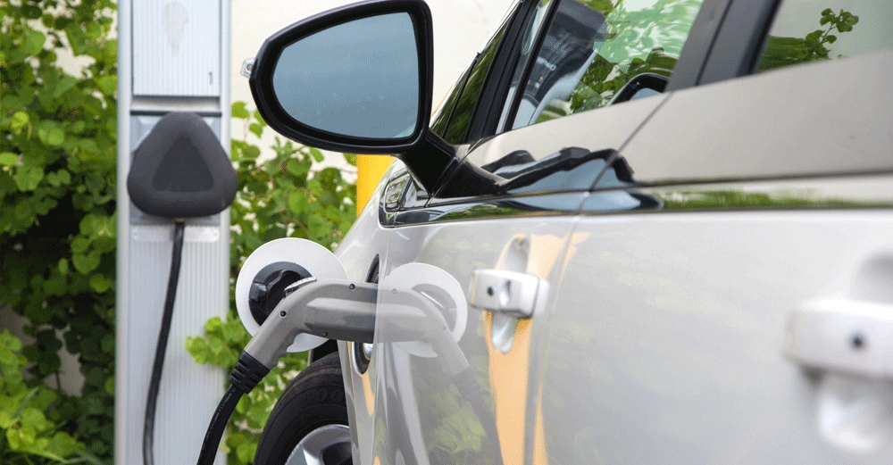 Ein Elektroauto wird aufgeladen an einer Ladestation im Freien umgeben von grünen Pflanzen