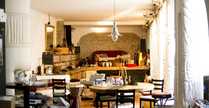 Galerie-Bild 7: Ein Wohnzimmer mit rustikaler Einrichtung zeigt Holzstühle und runde Tische Es gibt eine lange Arbeitsplatte vor einer Steinmauer Ein Sofa steht im Hintergrund umgeben von Lichtern und Dekorationen