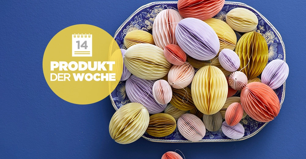 Papierbälle liegen auf einem verzierten Tablett in verschiedenen Farben, wie Gelb, Lila und Rot. Ein gelber Kreis zeigt die Aufschrift 14 PRODUKT DER WOCHE. Der Hintergrund ist blau.
