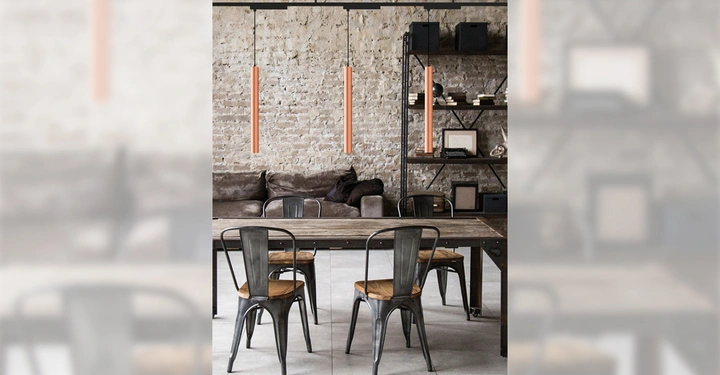 Ein Holztisch steht vor einem Sofa eine Regalwand voller Bücher und Dekorationen im Hintergrund eine Ziegelwand drei Hängeleuchten von der Decke hängen über dem Tisch.