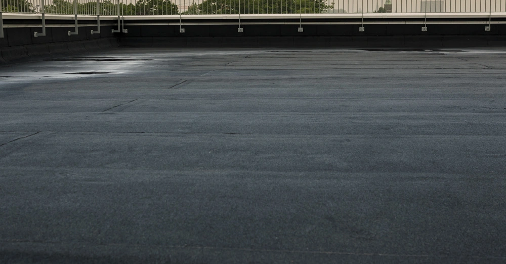 Flachdach mit grauem Belag Regenbogen am Himmel im Hintergrund Geländer und grüne Bäume am Rand des Flachdachs.