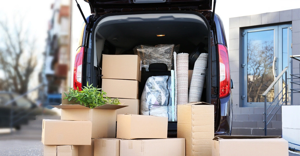 Hinteransicht eines Transporters voll mit Möbeln und Kisten. Davor stehen weitere Kisten auf dem Boden und warten darauf, eingeladen zu werden.