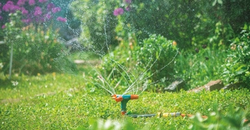 Ein Wassersprinkler versprüht Wasser im grünen Garten.