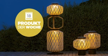 Große und kleine leuchtende Laternen auf Holzdeck im Freien beleuchten die Umgebung im Dunkeln. Text auf gelbem Kreis: 18 PRODUKT DER WOCHE. Im Hintergrund sind Büsche und ein dunkler Himmel zu sehen.