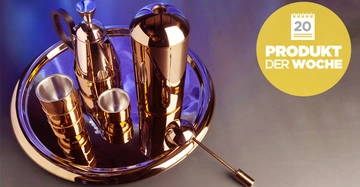 Ein Satz aus metallischen Getränkebehältern steht auf einem runden Tablett. Ein gelbes Symbol rechts zeigt den Text 20 PRODUKT DER WOCHE. Hintergrund blau-violett.