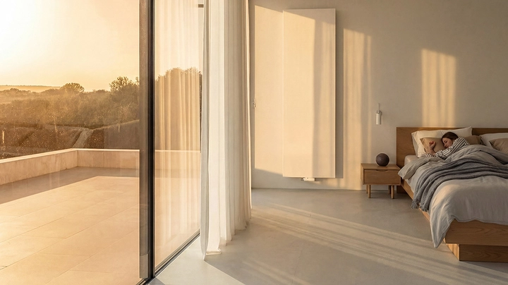 Galerie-Bild 1: Großes Schlafzimmer mit Ganzglasfront und Frau, die in einem Bett liegt. Morgensonne scheint rein.