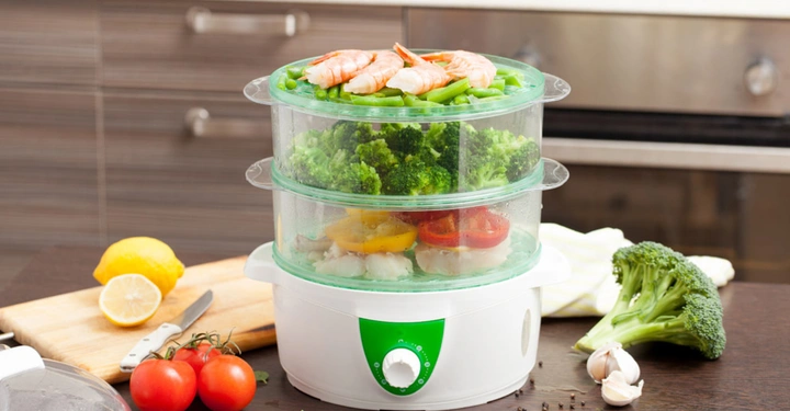 Dampfgarer in weiß und grün. Der Dampfgarerturm steht gut befüllt mit Gemüse, Fisch und Beilagen bereit zum Essen. 