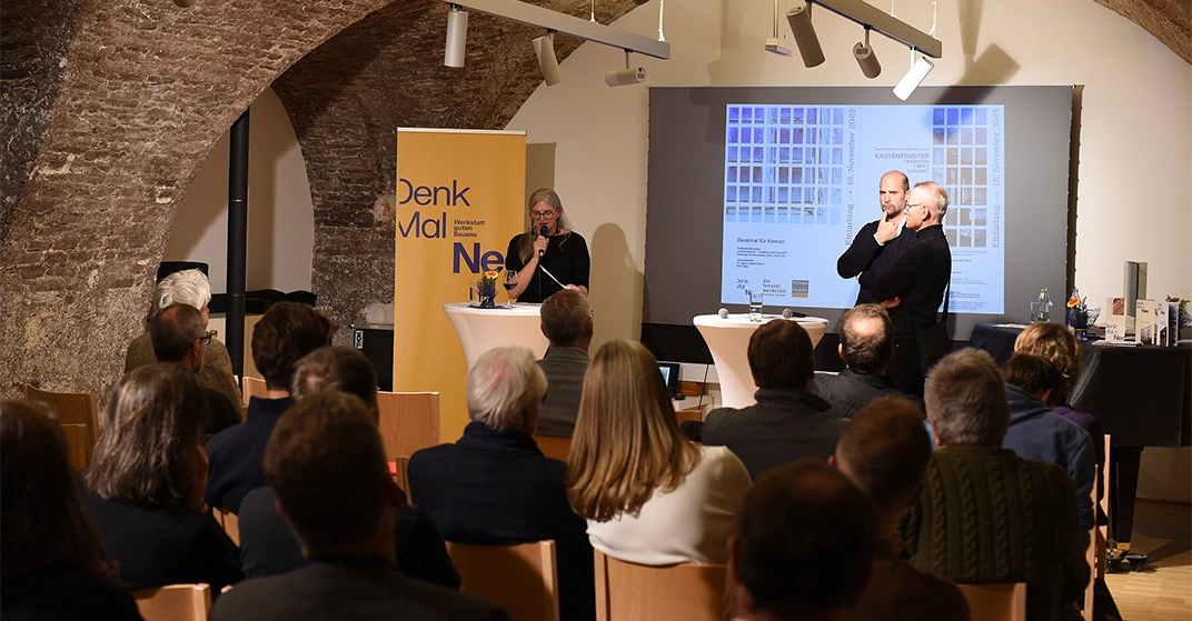 Eine Frau und zwei Männer von DenkMalNeo stehen auf einer Bühne vor Publikum.