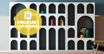 Regaleinheit zeigt dekorative Gegenstände Sitzmöbel im Vordergrund Gelber Kreis mit Text 32 PRODUKT DER WOCHE Wohnungseinrichtung modern gestaltet wandmontiert klar strukturiert helle und dunkle Farben verwendet