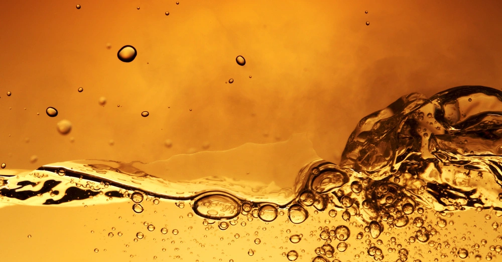 Blasen steigen in einer goldfarbenen Flüssigkeit auf dichter geschätzter Flüssigkeitshintergrund in einem warmen gelb-orangefarbenen Ton.