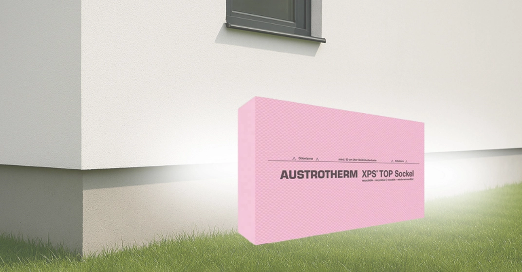 Darstellung der Austrotherm XPS® TOP Sockel Dämmplatte vor Hausfassade auf Gras