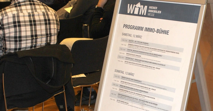 Galerie-Bild 18: Aufsteller zeigt Programmplan während Personen auf Stühlen sitzen. Text: WIENER IMMOBILIEN MESSE PROGRAMM IMMO-BÜHNE SAMSTAG 12.MÄRZ SONNTAG 13.MÄRZ Titel der Vorträge, Zeiten und Vortragende.