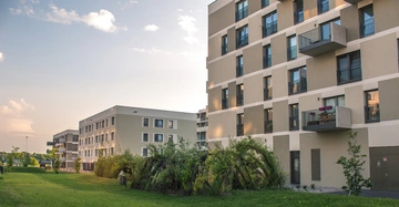 Mehrstöckige Wohngebäude mit Balkonen stehen nebeneinander im Freien bei Sonnenuntergang umgeben von Rasenflächen und Bäumen