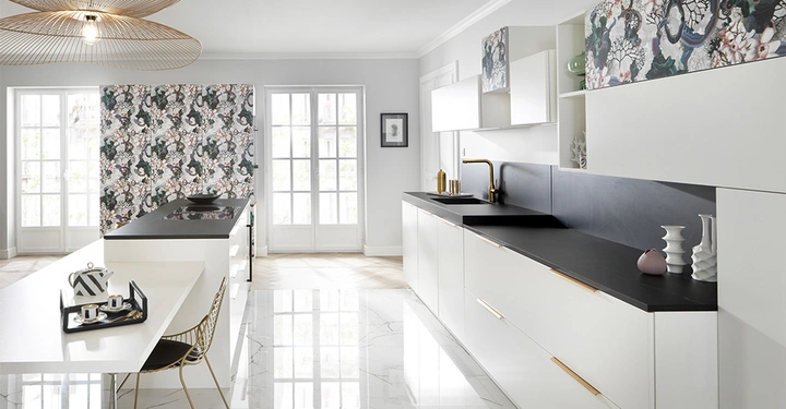 Moderne Küche mit weißen Schränken und schwarzer Arbeitsfläche im Sonnenlicht Goldener Wasserhahn und Dekorationen auf der Theke Zwei Fensterflügel und eine bedruckte Rückwand im Hintergrund Heller Marmorboden.