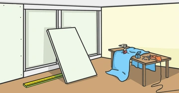 Eine große Platte lehnt in einem Raum an einer Wand bei Fenstern ein Maßstab liegt am Boden ein Arbeitstisch ist bedeckt mit Werkzeugen Stoff und einer Bohrmaschine.