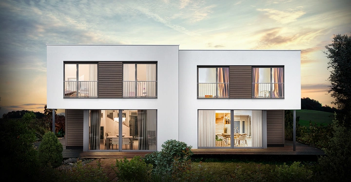 Modernes zweistöckiges Haus mit weißen Wänden und großen Fenstern beleuchtet von innen stehend in einem grünen Garten unter einem bewölkten Himmel bei Sonnenuntergang.