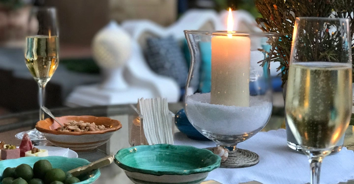 Kerzenlicht beleuchtet Snacks und gefüllte Champagnergläser auf einem gedeckten Tisch während ein gemütlich eingerichteter Bereich im Hintergrund zu sehen ist