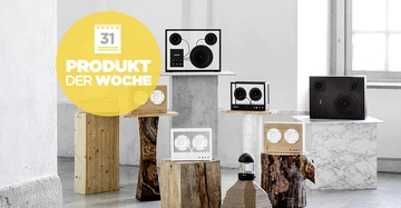 Lautsprecher stehen auf verschiedenartigen Podesten aus Holz und Stein in einer hellen Wohnung Produkt der Woche Text in einem gelben Kreis mit einem Kalender Symbol zeigt 31 an.