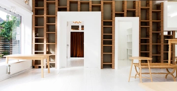 Leerer Raum mit Bücherregalen an der Wand Holztisch und Bank im Vordergrund durch große Fenster flutet Tageslicht herein Holzregale und weiß gestrichener Boden schaffen eine helle Atmosphäre.