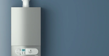 Gasgefeuerter Boiler hängt an einer blauen Wand arbeitet mit Anzeige auf 45 Grad und mehreren Anschlüssen darunter Ab- und Einschalter sowie Kontrollleuchten sind sichtbar.