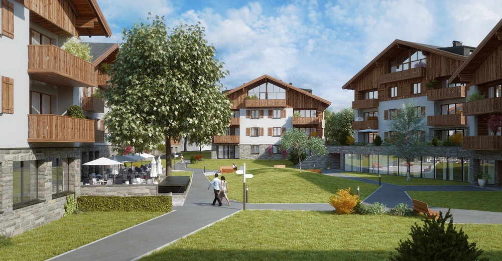 Zwei Personen spazieren auf einem Gehweg durch eine Wohnanlage mit modernen Häusern im alpinen Stil mit Holzbalkonen umgeben von Grünflächen und Bäumen an einem sonnigen Tag.