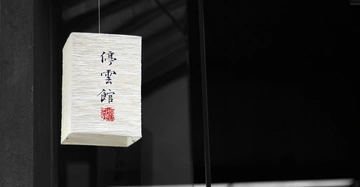Rechteckige Papierlaterne hängt an einer Schnur im Innenraum. Auf der Laterne stehen japanische Schriftzeichen. Der Hintergrund ist dunkel und unbeleuchtet.