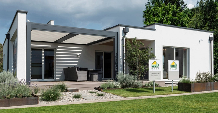 Ein modernes zweistöckiges Haus steht in einem gepflegten Garten mit Möbeln auf der Terrasse. Zwei Schilder vor dem Haus zeigen: "WOLF HAUS ELEGANCE 130 www.wolfhaus.at" und "WOLF KELLER".
