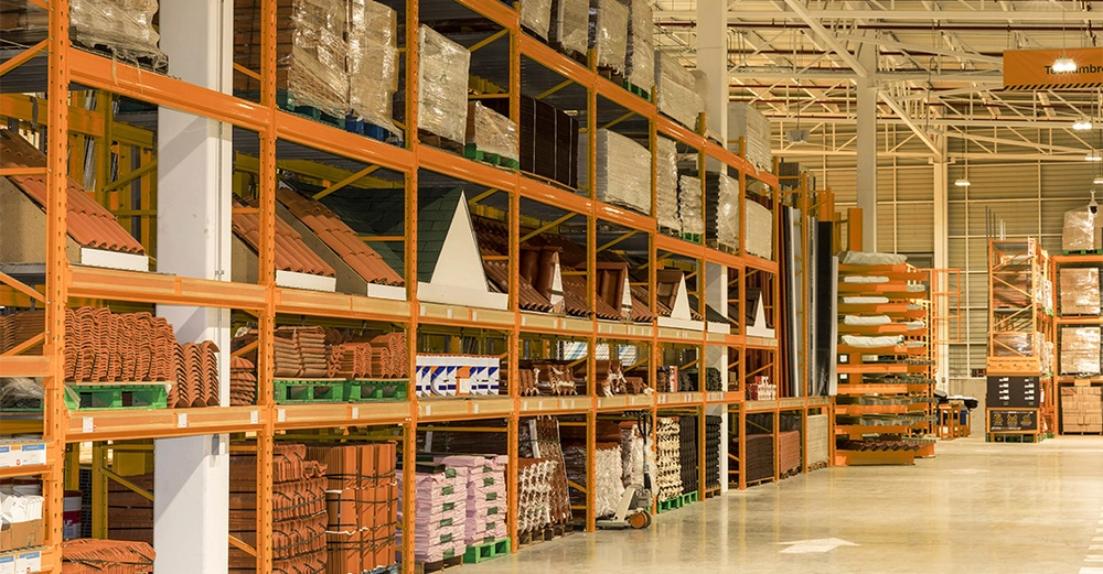 Regale mit Dachziegeln und Baumaterialien sind in einem großen, gut beleuchteten Lagerhaus angeordnet. Die Regale sind mehrstöckig und blitzsauber, mit verschiedenen Baumaterialien ordentlich gelagert.