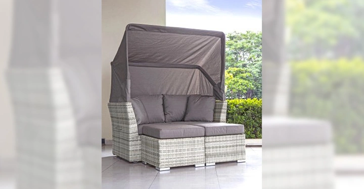 Galerie-Bild 9: Eine Korbgeflecht-Doppelliege mit grauen Kissen und einem hochgeklappten Sonnendach steht auf einer Terrasse neben einer Hecke und unter einem blauen Himmel.