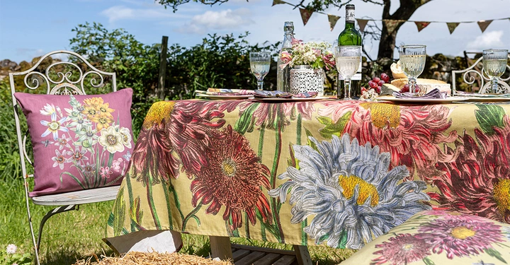 Wunderschöne florale Tischdecke in verschiedenen Altrosatönen liegt über Tisch im Garten. Servietten und Sitzkissen runden die Tischwäsche ab.