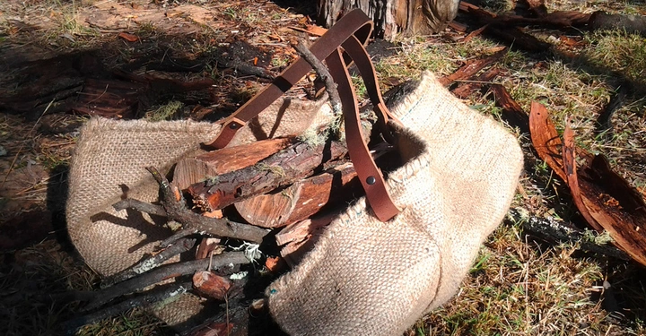 Ein Leinensack mit Holzscheiten und Zweigen liegt auf Grasboden im Freien umgeben von abgefallener Baumrinde und Zweigen