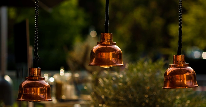 Drei hängende Kupferlampen leuchten nicht vor verschwommenem Hintergrund mit Pflanzen und Gegenständen im Freien.