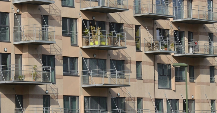 Galerie-Bild 4: Dunkelbeige Fassade eines großen Wohngebäudes mit Hängebalkonen aus Metall, die meisten Balkone sind leer, auf manchen stehen Topfpflanzen