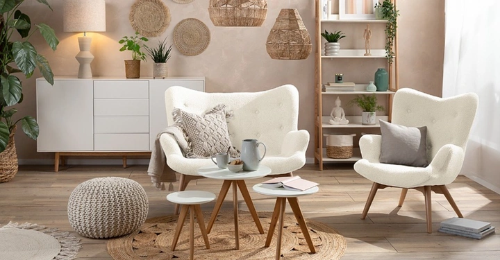 Gemütliches Wohnzimmer im Boho-Stil mit weißen Bouclé-Sesseln, Jute-Teppichen und geflochtenen Lampen. Pflanzen, ein weißes Sideboard und Holzmöbel in warmen Naturtönen schaffen ein harmonisches, lichtdurchflutetes Ambiente.