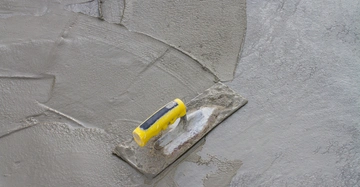 Kelle mit gelbem Griff liegt auf frisch gegossenem, glattem Beton, in einer Umgebung, die anscheinend eine Baustelle ist.