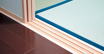 Schiebetüren öffnen sich zwischen einem dunkelbraunen Holzboden und einem hellen Raum mit Tatamimatten.