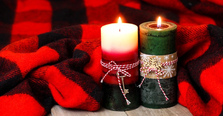 Zwei brennende Kerzen stehen nebeneinander auf einem Holztisch umgeben von einem rot-schwarz karierten Tuch.