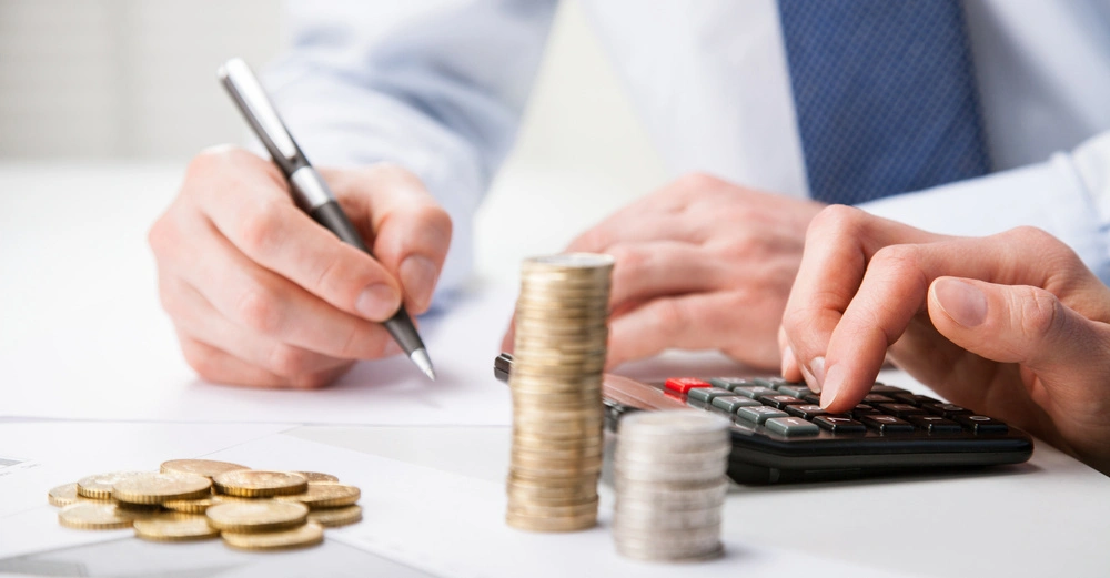 Hände stapeln Münzen und nutzen einen Taschenrechner auf einem Schreibtisch mit Diagrammen und Papieren in einem Büro.