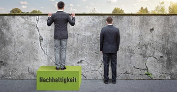 Mann steht auf grünem Block mit dem Text Nachhaltigkeit und blickt über eine graue Mauer während ein anderer Mann daneben auf dem Boden steht und die Mauer betrachtet im Freien mit Bäumen im Hintergrund